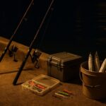 夜の堤防でタチウオを狙う釣りの雰囲気。常夜灯が海面に映え、ロッドと道具が並ぶ