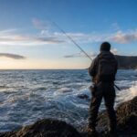 日本海の磯に立ちロッドを構えるアングラーの後ろ姿